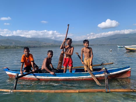 Four boys in a canoe enjoying a sunny day on a picturesque lake in Timor-Leste.