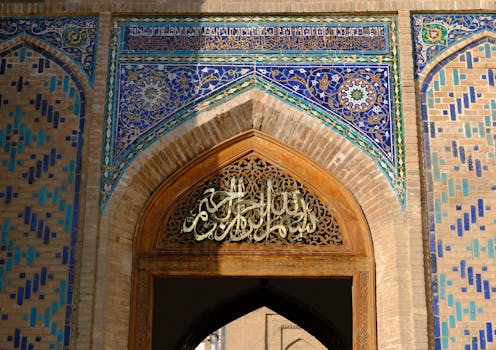 Intricate Islamic architecture with blue mosaic tiles and Arabic calligraphy on an arch.